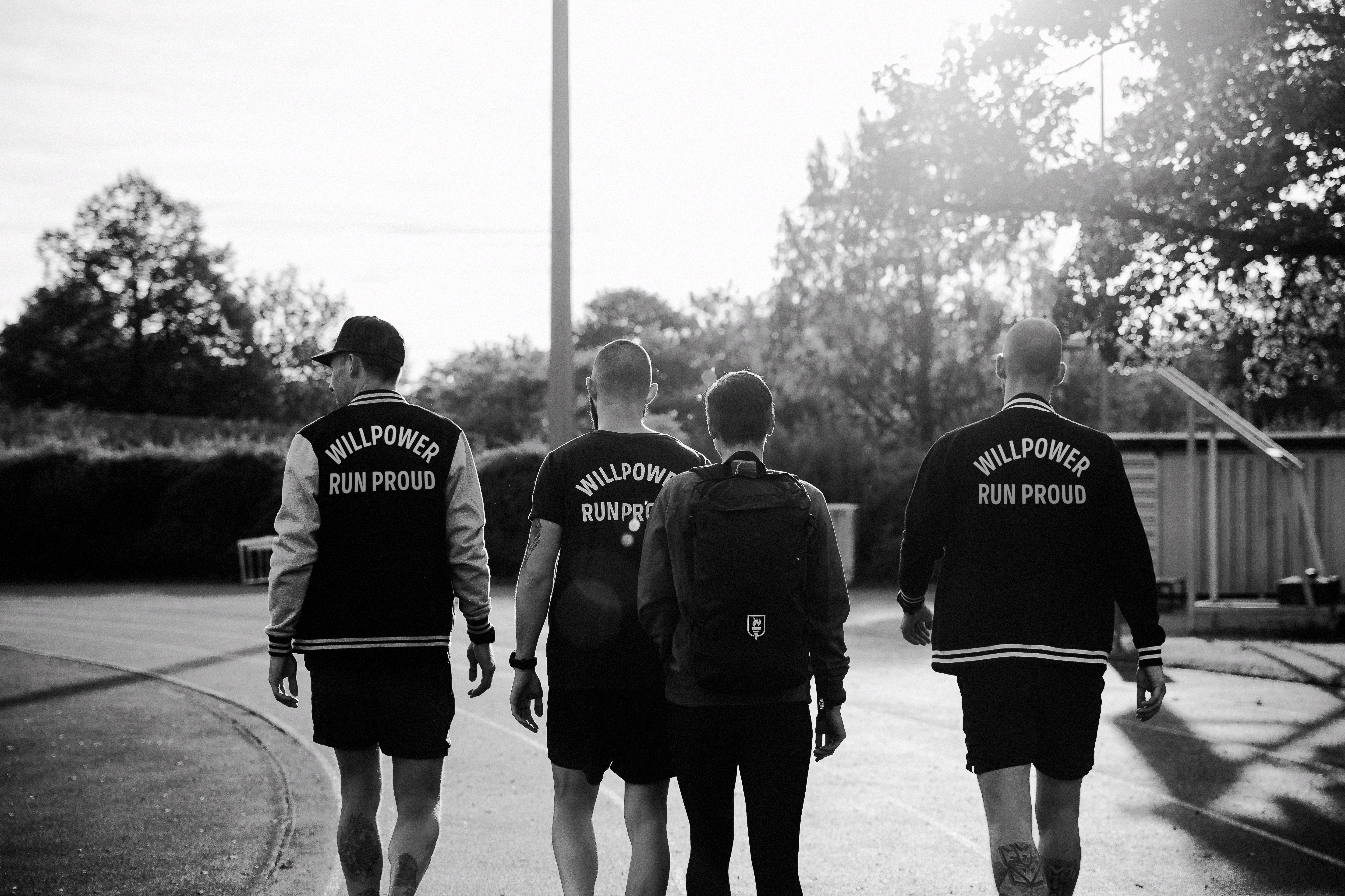 Four individuals wearing 'Willpower Run Proud' jackets walking outdoors.