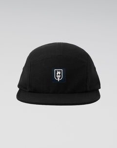 A black five-panel camp cap with a small rectangular embroidered patch on the front featuring a white flame and the word 'SUNRISE' on a dark navy background, set against a light gray gradient studio background.