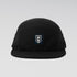 A black five-panel camp cap with a small rectangular embroidered patch on the front featuring a white flame and the word 'SUNRISE' on a dark navy background, set against a light gray gradient studio background.