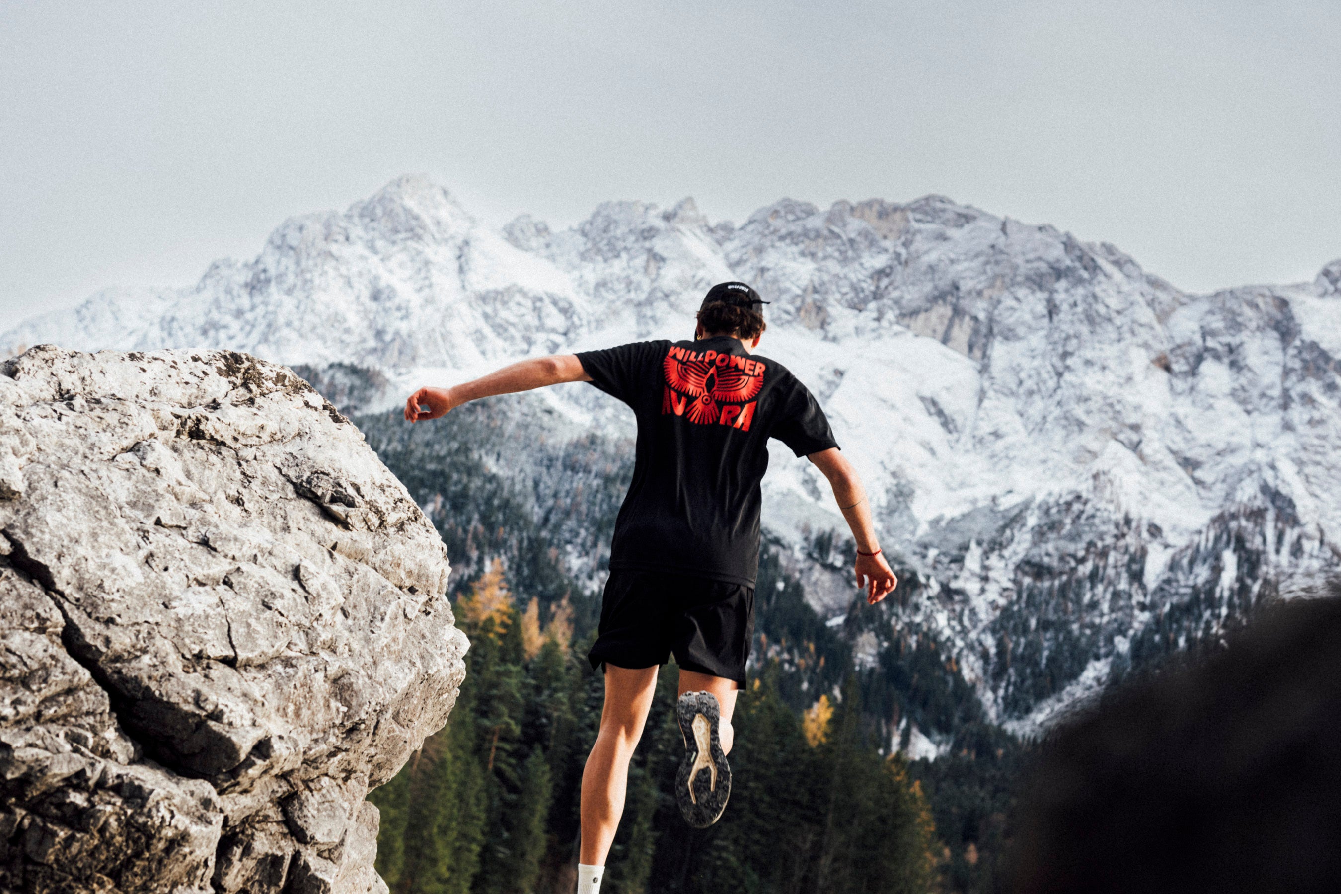 Person running on a rocky outcrop with snow-capped mountains in the background