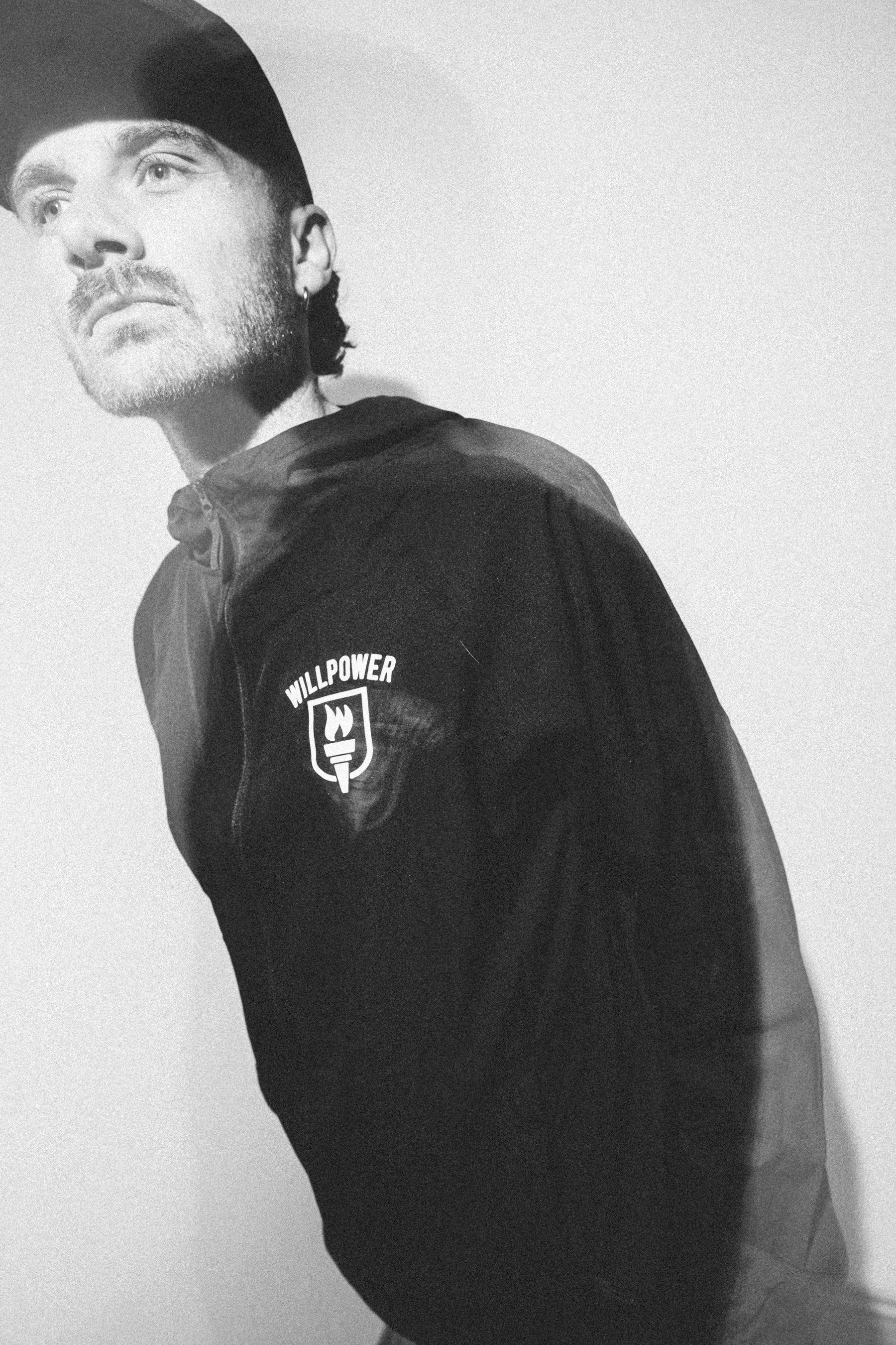 Person wearing a black hoodie with a logo on a plain background