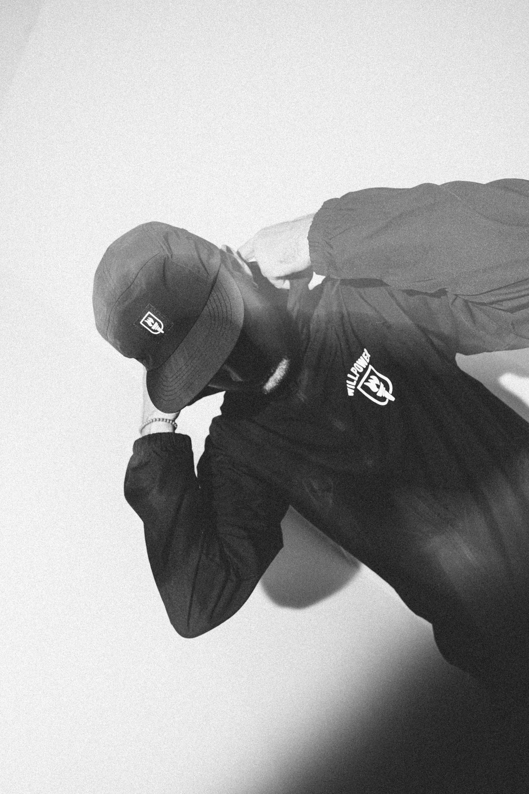 Person wearing a jacket and cap with brand logos on a light background