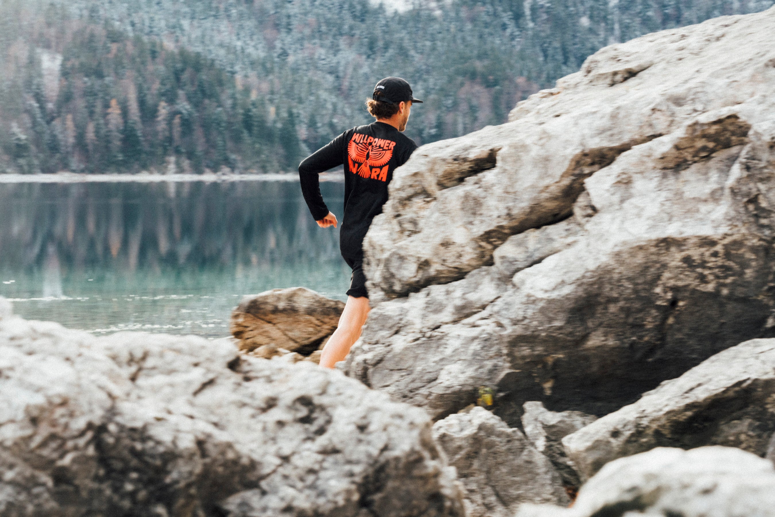 Person walking on rocks by a lake with mountains in the background