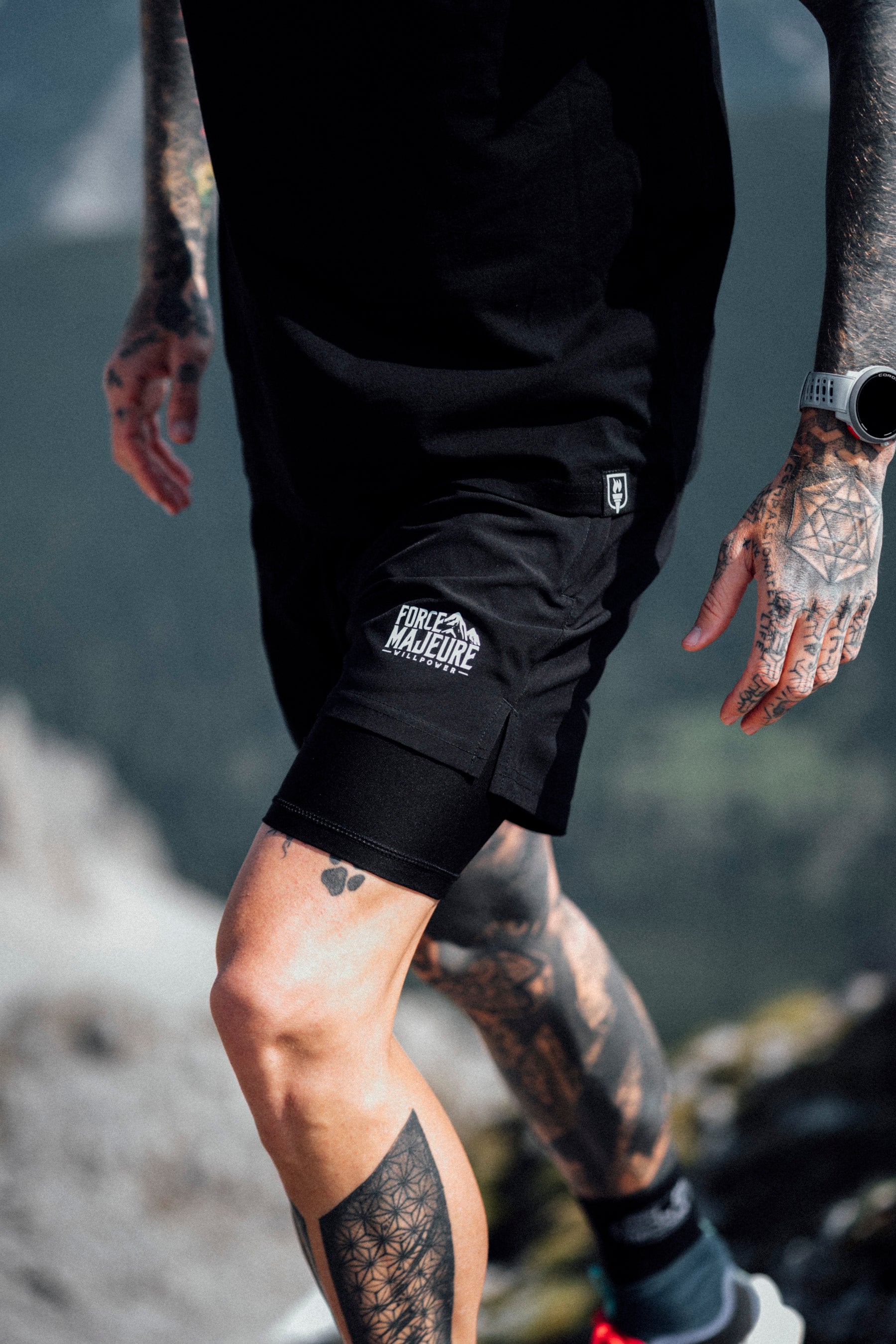 Person wearing black shorts with a logo, standing outdoors with a blurred natural background