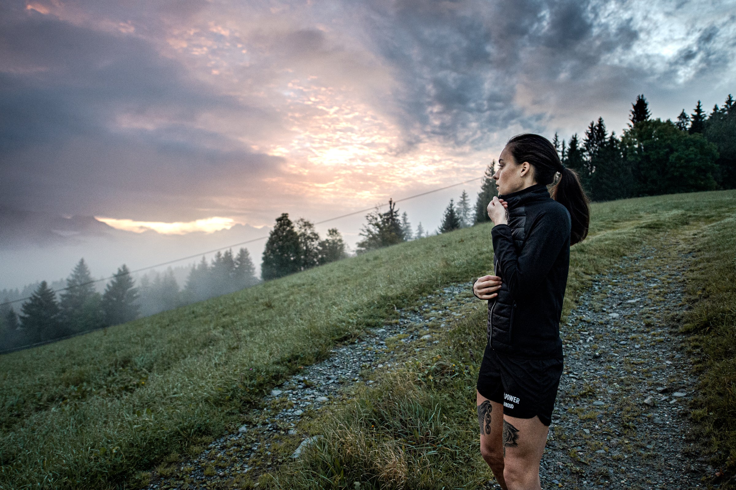 Person standing on a trail with a dramatic sky and mountains in the background